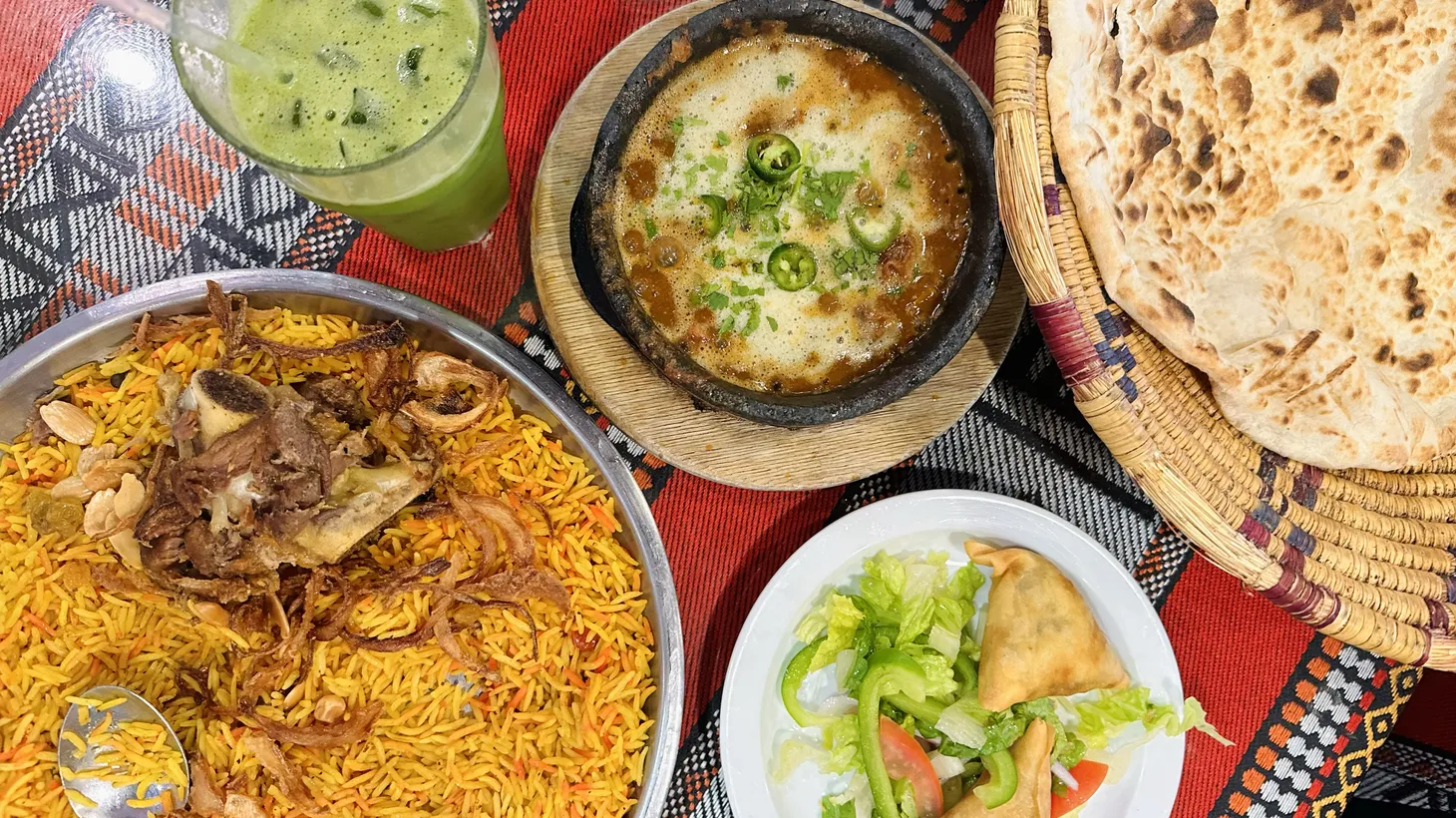 A platter of mandi with lamb, a glass of sweet mint and lemon juice, a bubbling pot of Hrada of Fahsah, a large round of flatbread and a couple of sambosas at Yemeni restaurant House of Mandi.