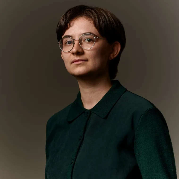 Person with short hair and glasses in a dark button down