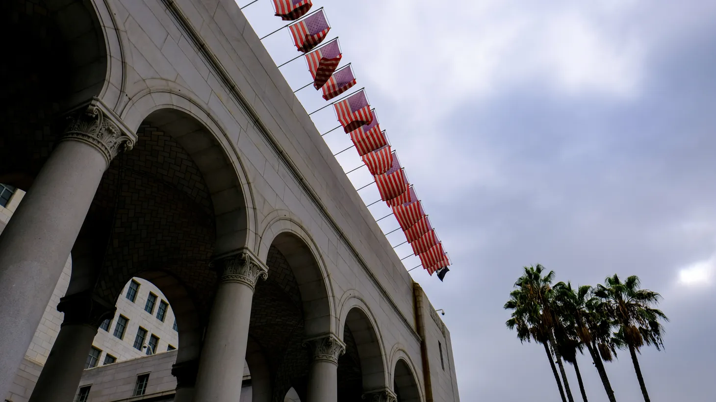 U.S. flags wave atop LA City Hall on a cloudy day, October 14, 2022. “Nobody is questioning the idea that a city that is half Latino should have more than four seats on the City Council, and that this might reinvigorate people to try and bring in politicians who might have a broader understanding, so that whatever coalitions that are built between the Latino politicians would not be … at odds with, say, a Black coalition, which is some of the stuff that we heard in those tapes,” says Jay Caspian Kang, staff writer for the New Yorker.