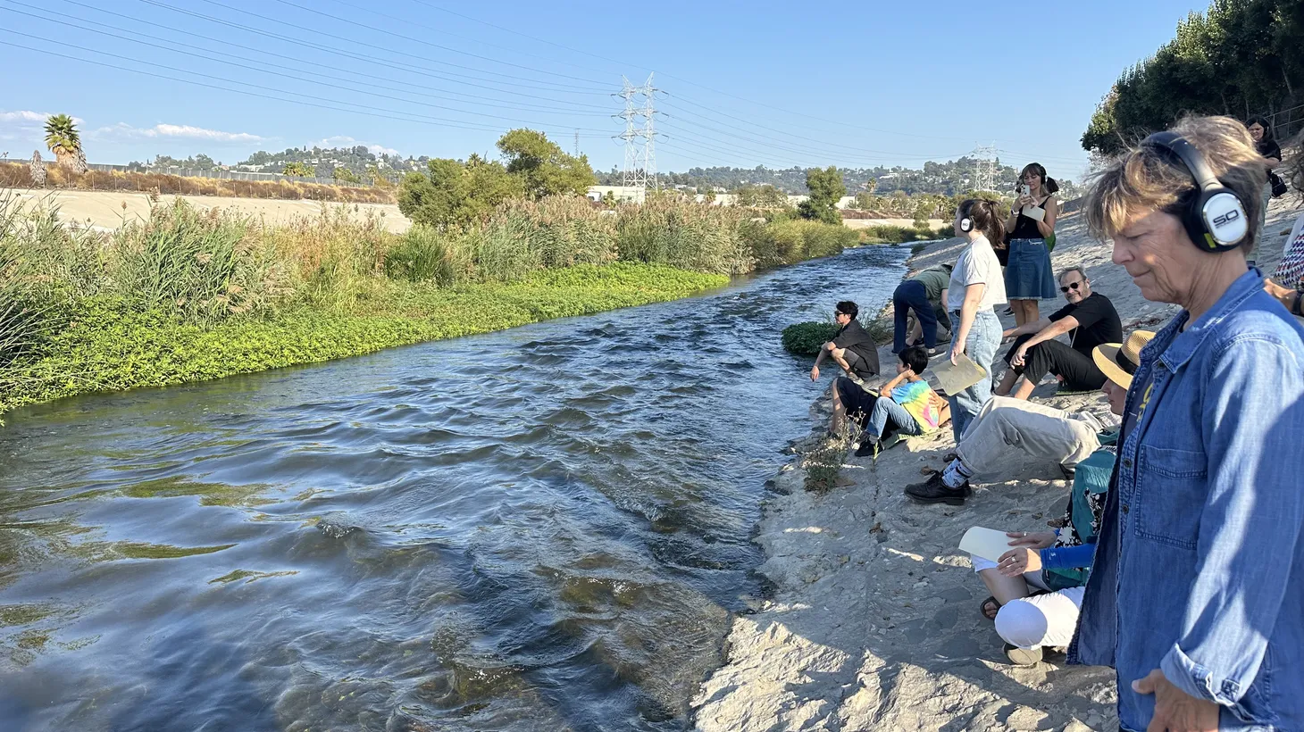 People wear headphones and sit along the edge of the LA River, just below the Glendale freeway in Frogtown, to immerse themselves in “What Water Wants.”